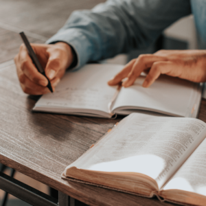 Une personne écrit sur un carnet, il a devant lui un guide grand ouvert.