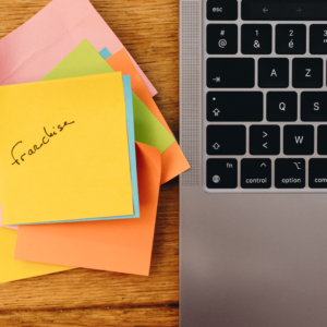 Une pile de post it au sommet de laquelle il est écrit Franchise, à côté d'un ordinateur.