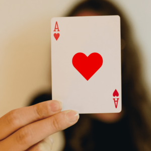 Une femme tient devant son visage un as de cœur.