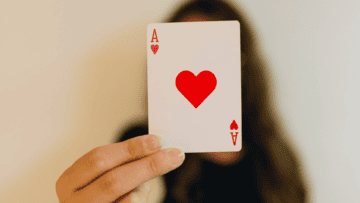 Une femme tient devant son visage un as de cœur.