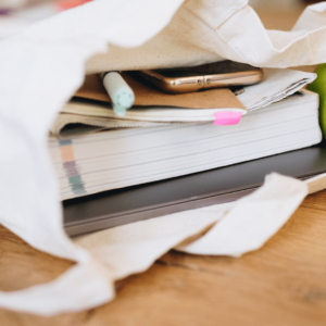 Un sac en tissu dans lequel il y a une pomme, un livre, un ordinateur, un carnet et un téléphone.