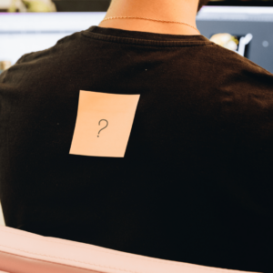Un postit orange avec un point d'interrogation dessus, collé sur le dos d'un collaborateur.