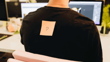 Un postit orange avec un point d'interrogation dessus, collé sur le dos d'un collaborateur.