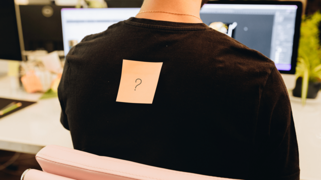 Un postit orange avec un point d'interrogation dessus, collé sur le dos d'un collaborateur.