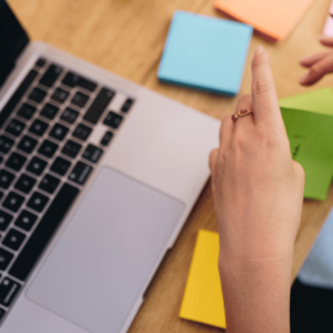 Une femme écrit quelque chose sur un post it devant son ordinateur.