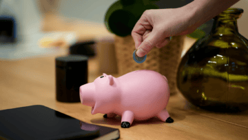 Une personne met une pièce de 2 euros dans un cochon rose.