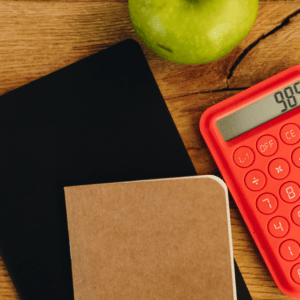 Une calculatrice rouge accompagnée d'un carnet et d'une pomme.