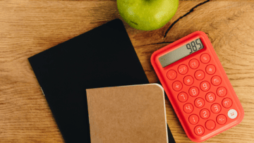 Une calculatrice rouge accompagnée d'un carnet et d'une pomme.