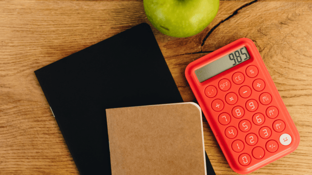 Une calculatrice rouge accompagnée d'un carnet et d'une pomme.