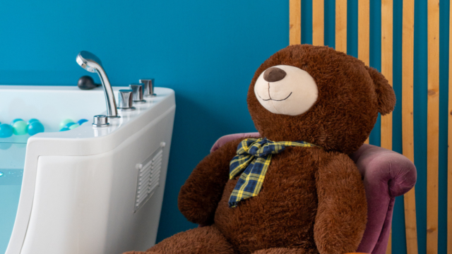 Un ours en peluche installé à côté d'une baignoire.