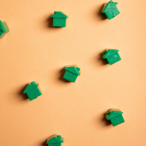 Zoom sur des maisons vertes de Monopoly éparpillées sur un fond orange.