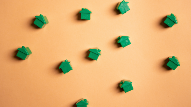 Zoom sur des maisons vertes de Monopoly éparpillées sur un fond orange.