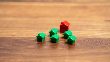 Cinq maisons vertes de Monopoly et une grosse rouge sur une table.