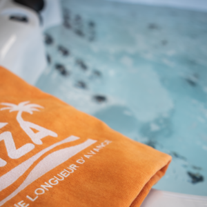 Au bord d'un jacuzzi, une serviette orange sur laquelle il y a écrit Piscines Ibiza.
