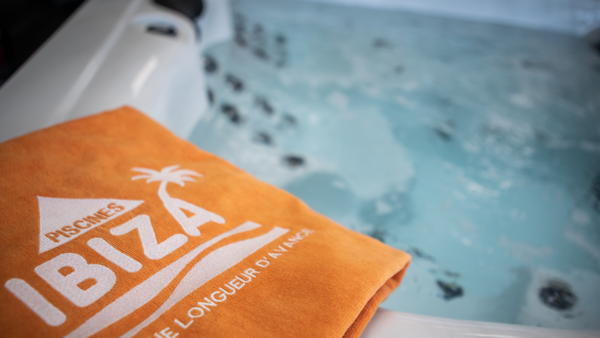 Au bord d'un jacuzzi, une serviette orange sur laquelle il y a écrit Piscines Ibiza.