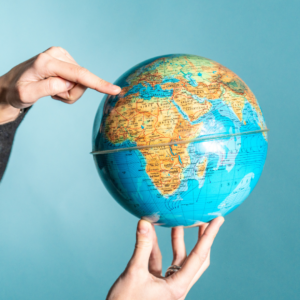 une main qui pointe un pays sur le globe