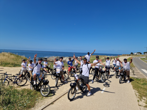 Equipe de la franchise Ecolave posant sur des vélos en bord de mer