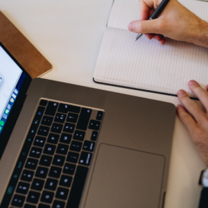 une personne qui écrit sur un carnet, un ordinateur sur la table