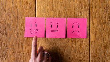 Sur une table en bois, trois post it représentent trois émotions : la joie, neutre, la colère. Un doigt pointe le post it joyeux.