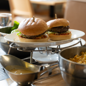 Sur une table de restaurant, il y a deux burgers posés sur une assiette et des frites dans un bol.