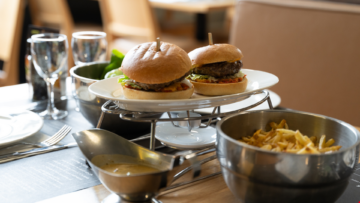 Sur une table de restaurant, il y a deux burgers posés sur une assiette et des frites dans un bol.
