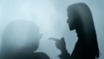 En ombre chinoise, une femme pointe du doigt une autre femme.