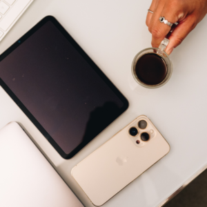Une tablette, un téléphone, un ordinateur et une tasse de café posés sur une table blanche.