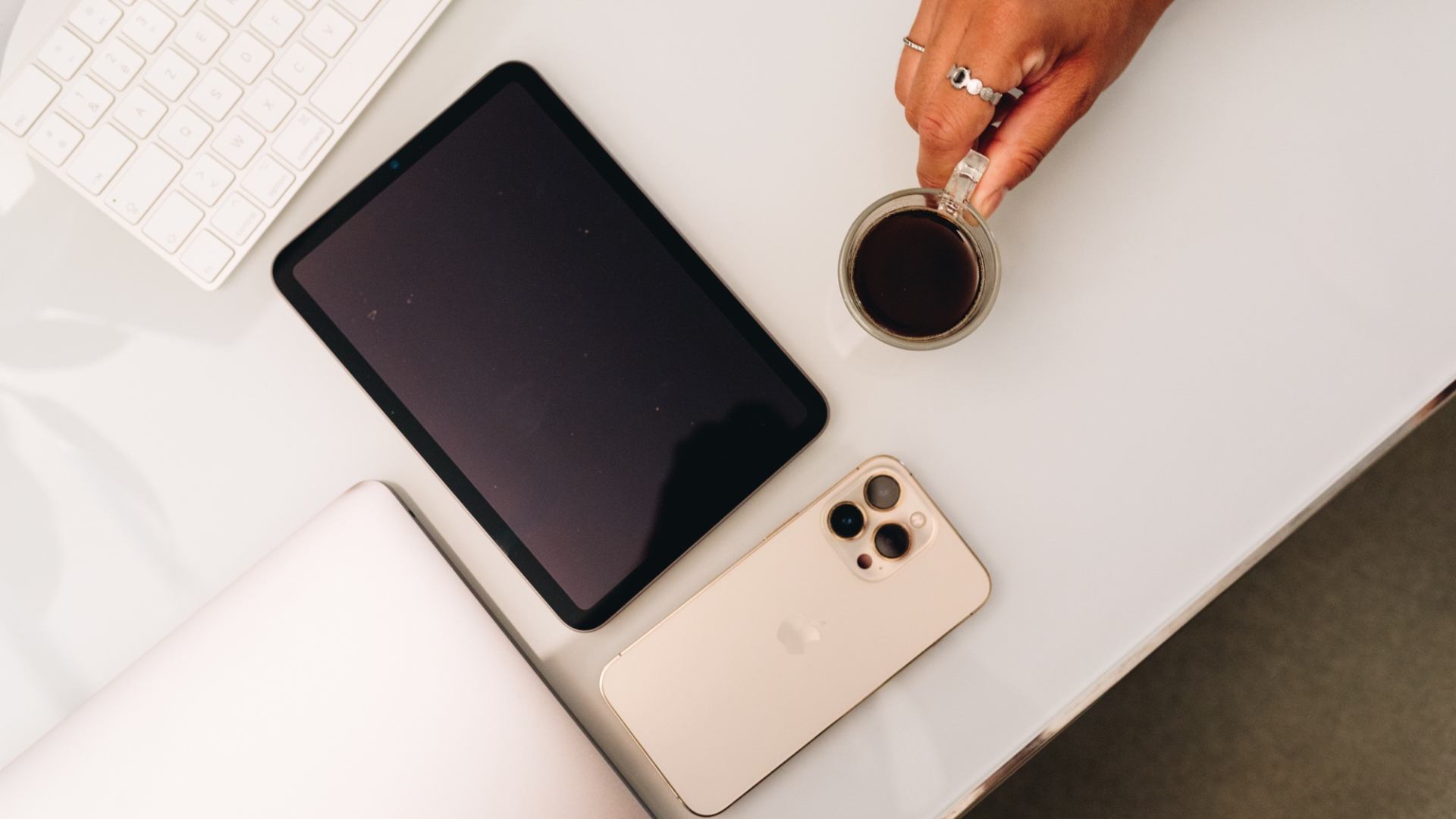 Une tablette, un téléphone, un ordinateur et une tasse de café posés sur une table blanche.