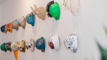 Des casques de chantier customisé accrochés à un mur blanc.