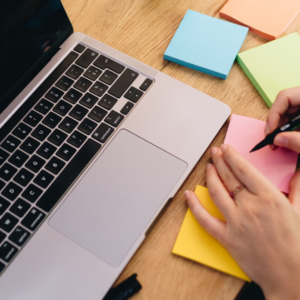 Une femme écrit sur un post it devant son ordinateur ouvert.