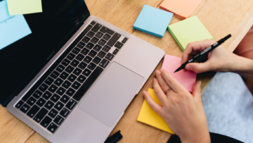 Une femme écrit sur un post it devant son ordinateur ouvert.