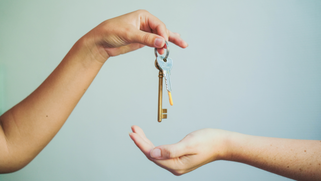 Sur un fond bleu gris, une main donne des clés à une autre.