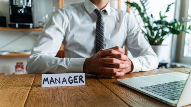 Un homme assis à son bureau avec un chevalet "Manager" posé devant lui.