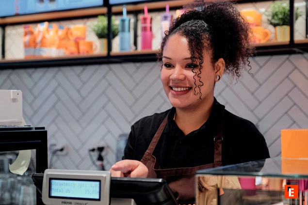 Femme souriante derrière un comptoir de café.