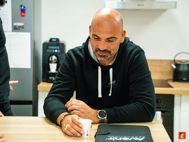 Hombre sonriente con taza en una mesa.