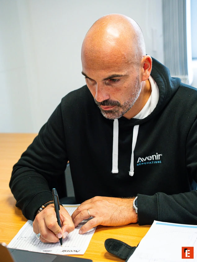 Persona escribiendo en una hoja junto a una laptop.