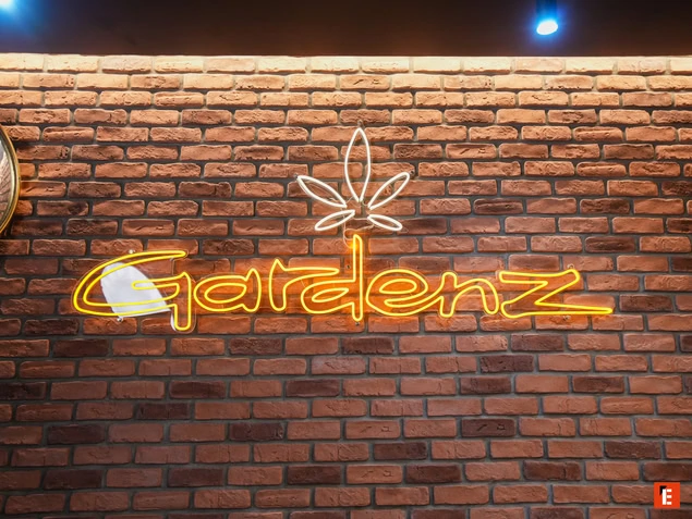 Logo lumineux GardenZ sur mur en briques.