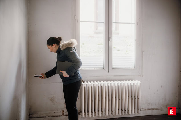Femme examine un mur avec son téléphone.