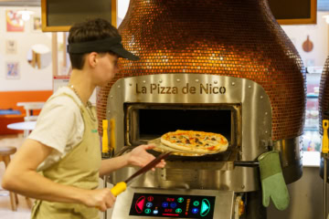 Une jeune homme entrain d'enfourner une pizza dans un four