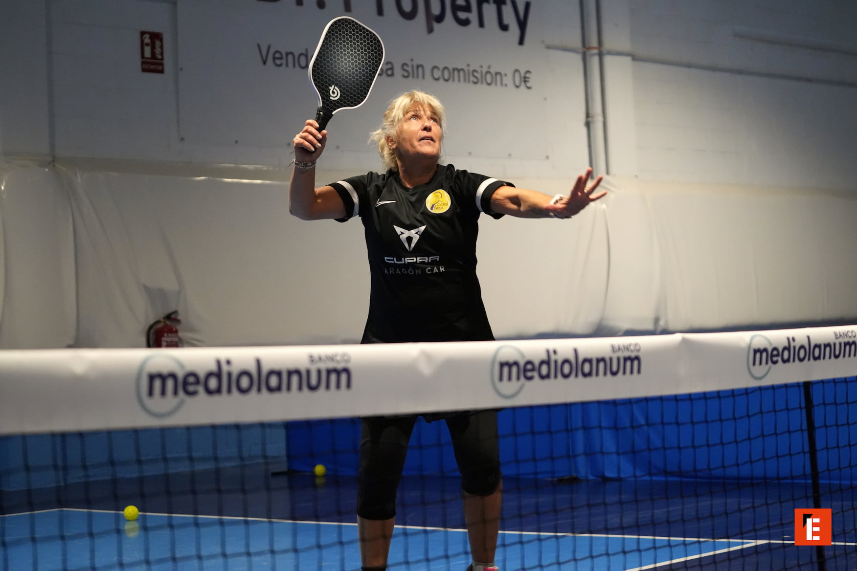 Mujer juega padel en una cancha interior.