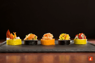 Cinq sushis colorés sur une assiette noire.