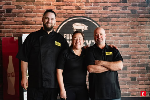 Trois employés souriants devant un mur en briques.