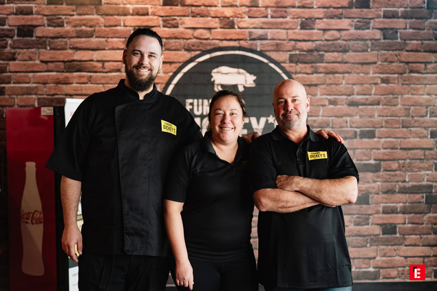 Trois employés souriants devant un mur en briques.