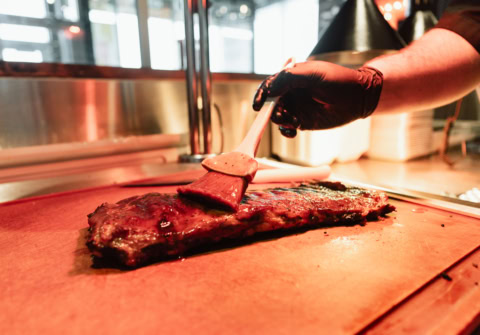 Focus sur une main entrain de mettre de l'huile au pinceau sur une viande