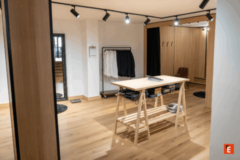 Tienda de ropa con espejo y estantes de madera.