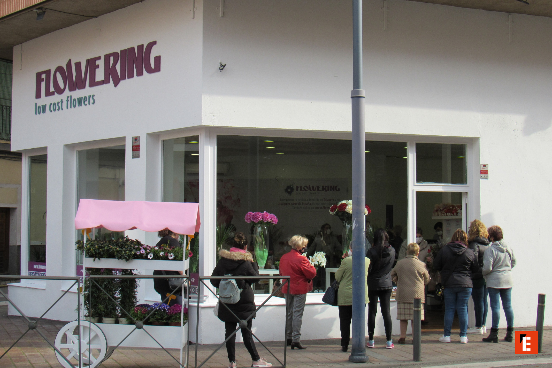 Tienda de flores con clientes en fila.