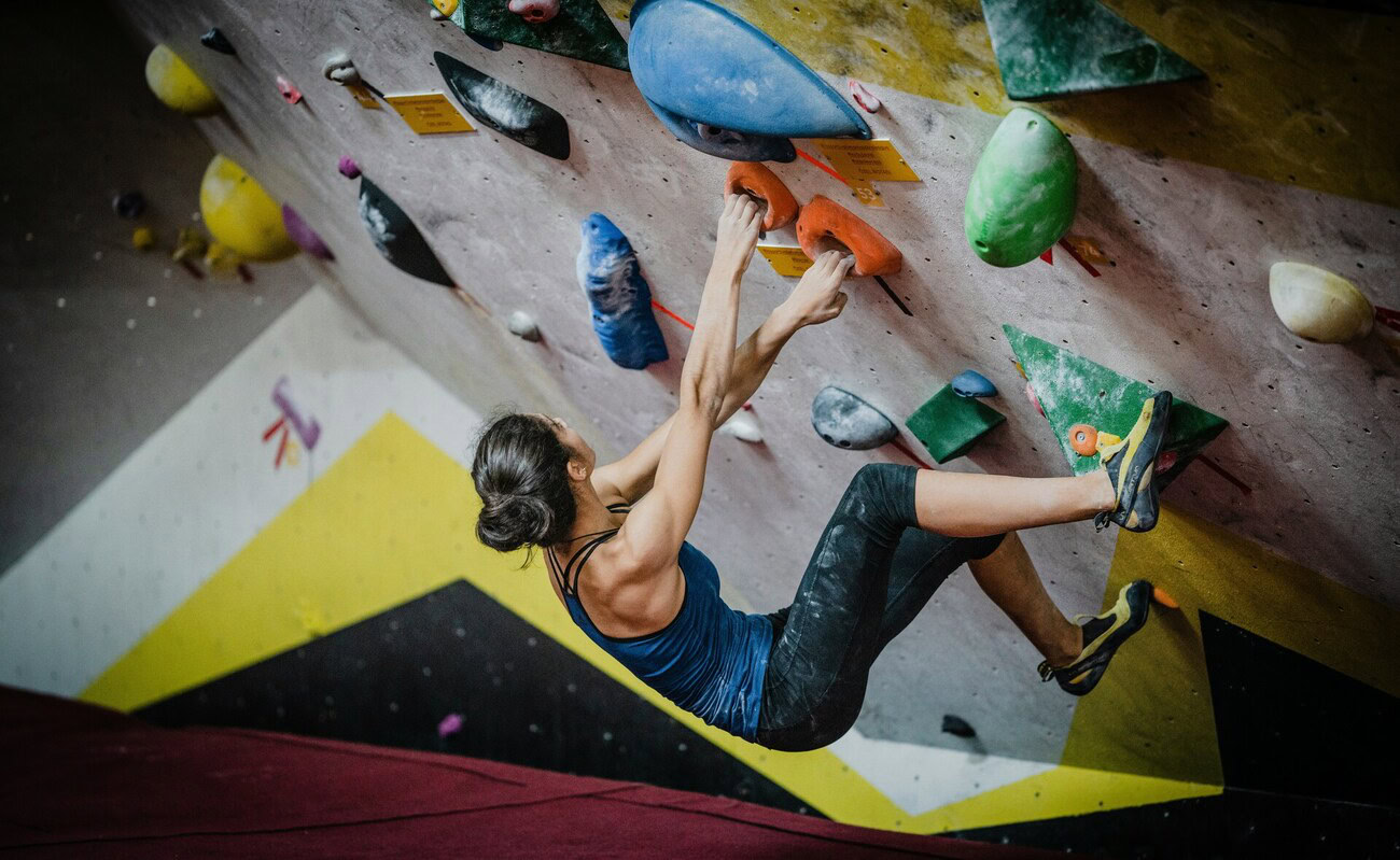 grimpeuse en dévers sur mur d’escalade coloré