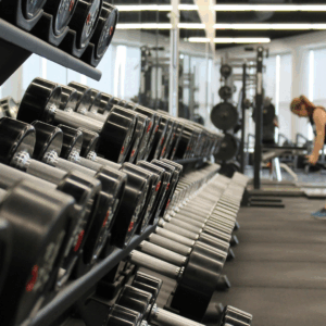 Inside of a gym, with a lady working out in the background