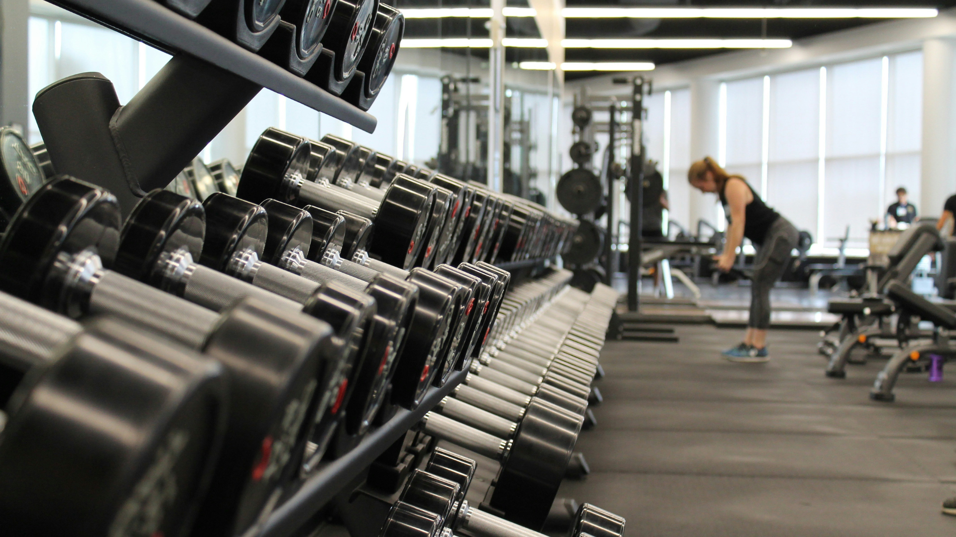 Inside of a gym, with a lady working out in the background