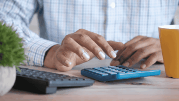 close up of a man's hands next to a calculator and a keyboard. the man's wearing a shirt
